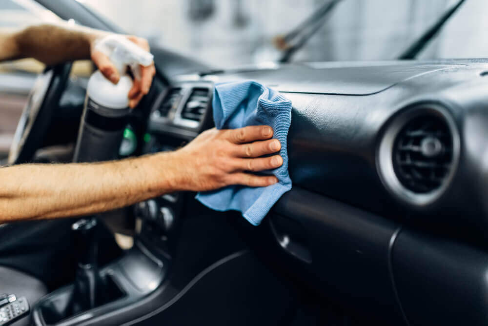 a car detailing Ballarat worker wiping down the interor of a car's dash board with a blue microfiber cloth and holding a spray bottle