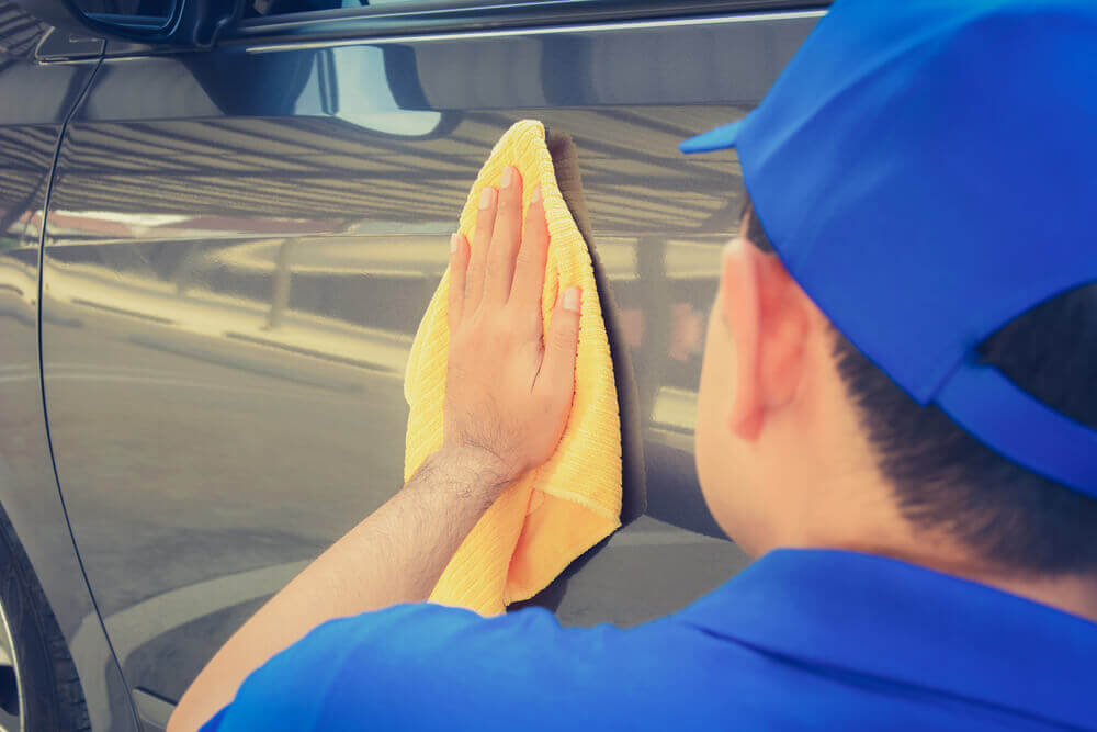 an exterior detail cleaner wiping down the side of a silver car with a yellow microfiber cloth