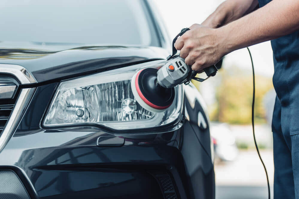 image of a car detailing Ballarat cleaner using a buffing wheel on the headlight of a black car that has protective tape around the paint