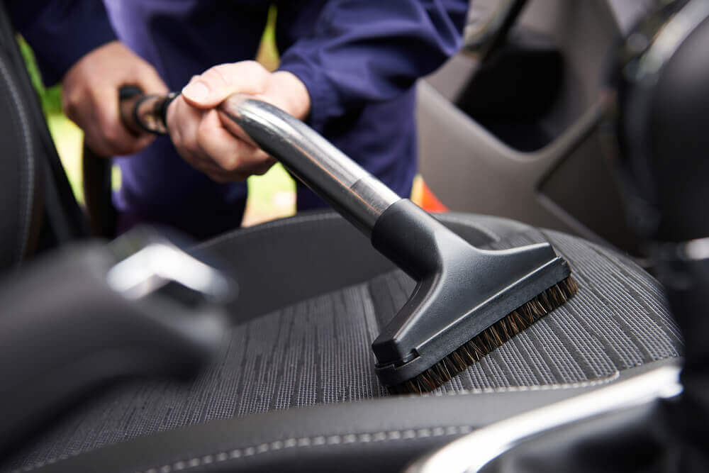 an interior detail worker vacuuming the drivers seat of a vehicle with an interior car vacuum 