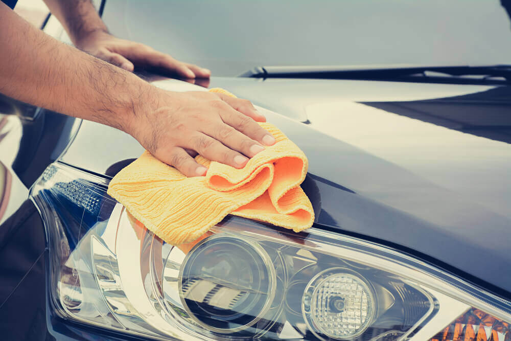 image of a car detailing Ballarat worker wiping down the headlight clean of a black car with a yellow microfiber cloth